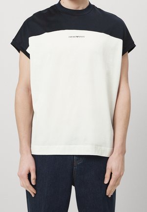 Short-sleeve t-shirt with a navy top and white bottom section. Features a round neckline and a logo print on the chest. Cotton material.