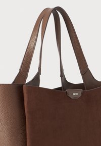 Bruine leren tote bag met een gestructureerd lichaam, gladde accenten en dubbele platte handvatten. Heeft een minimalistisch ontwerp en DKNY-logo detail.