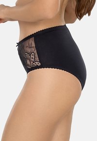 Mutandine nere a vita alta con pannelli laterali in pizzo trasparente con motivi floreali. Bordo ondulato e dettaglio a fiocco decorativo sul davanti.