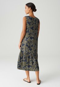 Sleeveless green camo dress with a tiered hem, featuring a round neckline and back button closure. Made from lightweight fabric.