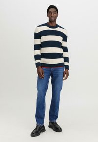 Strickpullover mit navy- und cremefarbenen horizontalen Streifen, Rundhalsausschnitt, gerippte Bündchen, kombiniert mit blauen Jeans und schwarzen Lederschuhen.