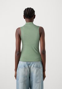 Grøn ærmeløs top med høj hals, lavet af et glat stof. Sæt sammen med lyseblå baggy jeans med baglommer.