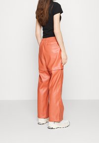 Peach leather wide-leg pants with an elastic waistband and snap buttons, paired with a fitted black t-shirt and white sneakers.