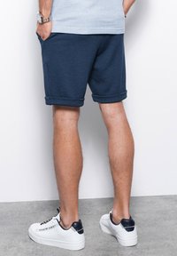 Námořnické modré bavlněné šortky s ohrnutými manžetami, doplněné o bílé tenisky s námořnickými akcenty a viditelnými tkaničkami. Stříbrné hodinky na zápěstí.