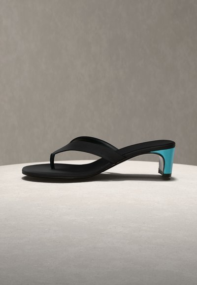 Μαύρο σανδάλι σαγιονάρα με χαμηλό μεταλλικό μπλε τετράγωνο τακούνι, τοποθετημένο σε ανοιχτή επιφάνεια με απλό φόντο.