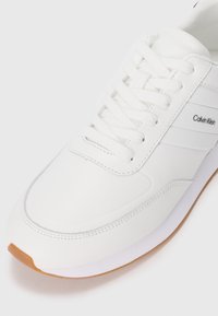 Weißer Sneaker aus glattem Leder, mit abgerundetem Zehenbereich, Schnürsenkeln und dezentem Logo-Detail. Gummisohle mit kontrastierendem braunem Zehenteil.