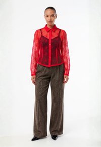 Red sheer lace blouse with floral pattern, button-down front, and collar. Paired with metallic, textured brown wide-leg trousers and pointed heels.