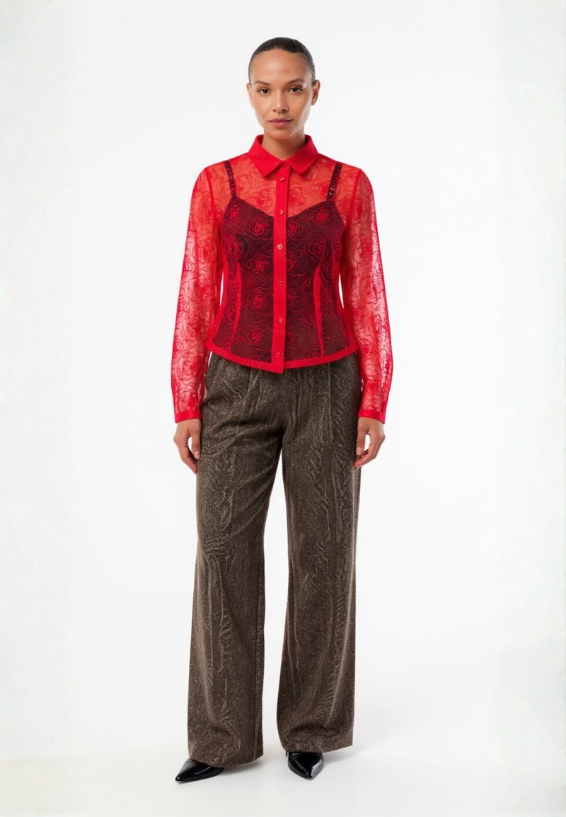 Red sheer lace blouse with floral pattern, button-down front, and collar. Paired with metallic, textured brown wide-leg trousers and pointed heels.