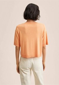 Maglione corto a maniche corte di colore arancione chiaro, realizzato in un materiale knit morbido. Presenta un collo rotondo e un design semplice.