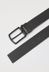 Μαύρη υφασμάτινη συνθετική ζώνη με ματ φινίρισμα, που διαθέτει ορθογώνια μεταλλική πόρπη και πέντε ρυθμιζόμενες τρύπες για διάσταση.