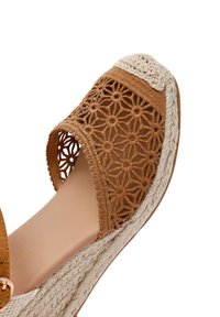 Zapato de esparto tejido en tono marrón con patrones florales recortados, parte superior texturizada y suela gruesa de yute. Punta redonda con una plantilla ligera y suave.