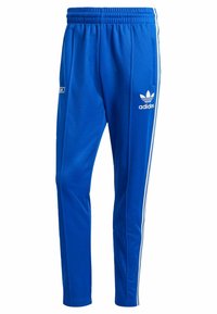 Blå Adidas träningsbyxor med vita ränder på sidorna, elastisk midja, sidan fickor och Adidas-logotyp på höger lår.