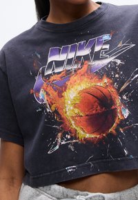 Μαύρο κοντομάνικο t-shirt με πολύχρωμο σχέδιο ενός μπασκετικού μπαλάκι περιβαλλόμενο από φλόγες, με την επιγραφή «NIKE» πάνω σε έντονα, πολύχρωμα γράμματα.