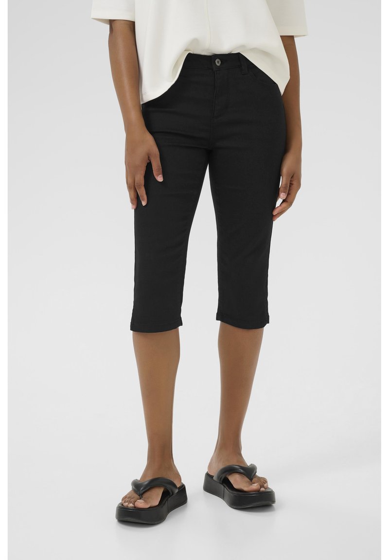 Jean noir coupé en denim extensible avec une coupe ajustée, présentant un style cinq poches et une taille mi-haute. Associés à des sandales à glissière noires.