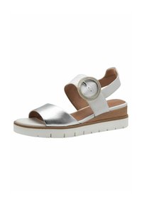 Sandal in metallo argento con una larga fascia alla punta, fascia bianca alla caviglia e un accento circolare. Suola a zeppa con dettagli marroni texturizzati.