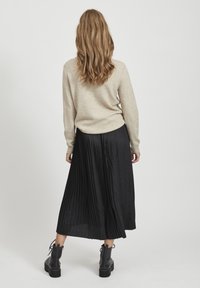 Beige wollen trui gecombineerd met een zwarte geplooide midi-skirt. Zwarte enkellaarsjes met dikke zolen. Textuurcontrasten tussen trui en rok.