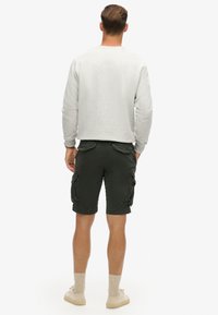 Sweatshirt gris clair associé à un short cargo vert foncé avec poches latérales. Des chaussures beiges et des chaussettes de cheville texturées complètent la tenue.
