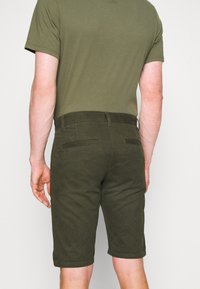 Shorts vert olive en tissu texturé, dotés de poches arrière et d'une ceinture lisse, associés à un haut à manches courtes assorti.