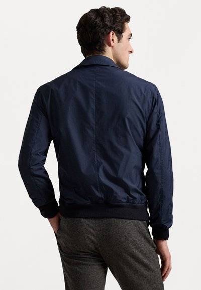 Ναυτικό μπλε bomber jacket με λεία, γυαλιστερή υφή, ριμπ μανσέτες και ζώνη, απεικονιζόμενο από πίσω με ελάχιστες λεπτομέρειες.