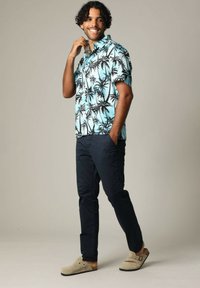 Kortebloesem met palmprint in lichtblauw, marineblauwe broek en beige klompen. Relaxte pasvorm, knopen op het shirt en zijzakken op de broek.