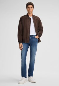 Brązowa zamszowa bomberka z zamkiem z przodu, prążkowanymi mankietami i gładką fakturą, w zestawieniu z niebieskimi dżinsami i białymi trampkami.