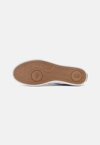 Gumowa podeszwa sportowa z wzorem jodełki, w kolorze brązowym z wytłoczonym logo "Polo". Biała podeszwa środkowa, zaokrąglony kształt noska.