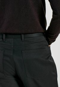 Black tailored trousers with a smooth texture, featuring two back pockets with subtle stitching and a waistband with belt loops.