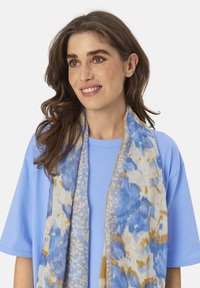 Lightweight scarf in blue, cream, and gold hues; features floral patterns; drapes softly around the neck; made of a soft, breathable fabric.