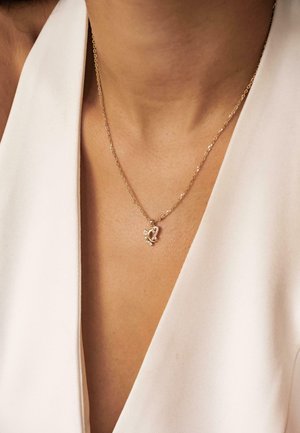 Gold chain necklace with a heart-shaped pendant, featuring decorative accents and a polished finish, resting on bare skin.