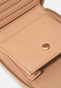 Intérieur de portefeuille en cuir beige clair avec des emplacements pour cartes, une fermeture à bouton-pression et un bord zippé. Texture lisse avec des coutures contrastées.