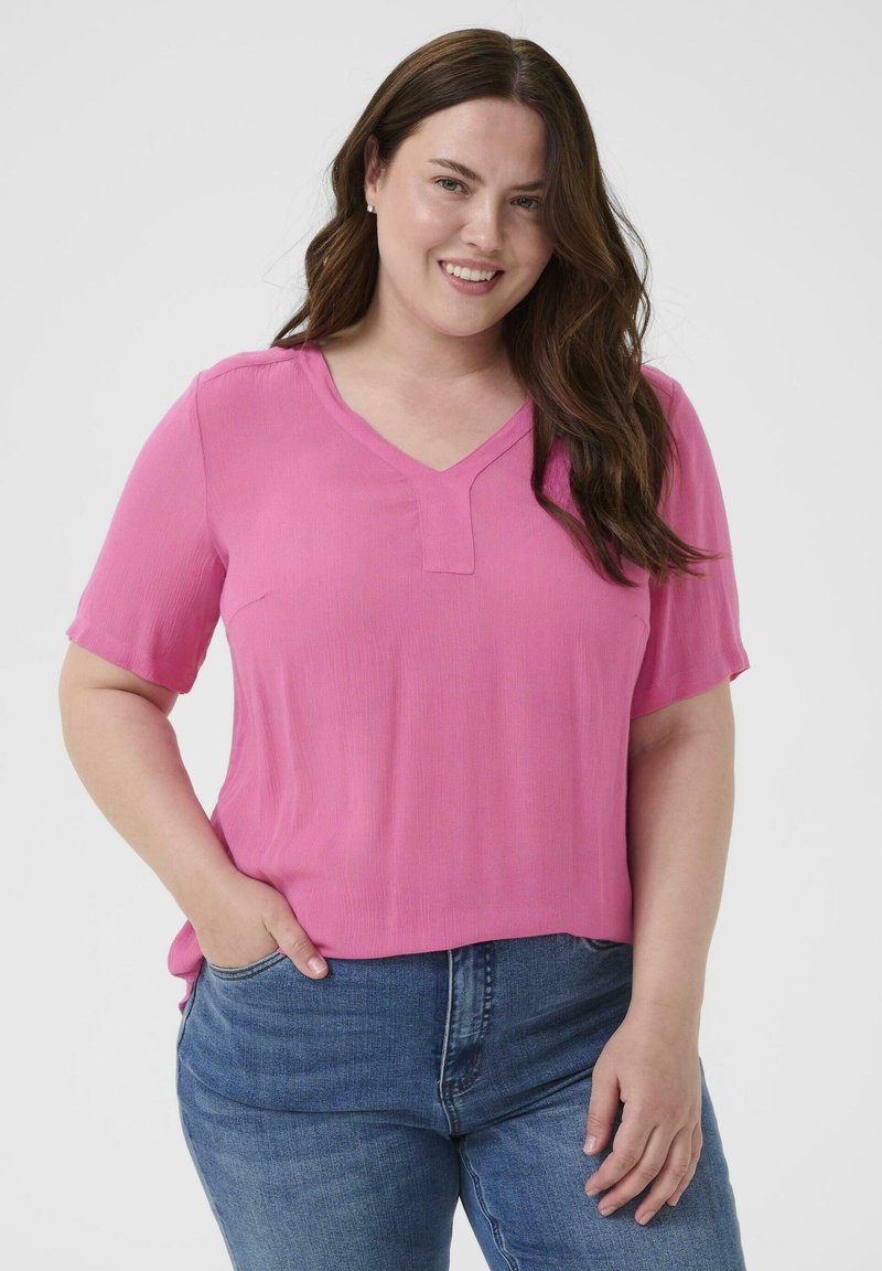 Haut rose à manches courtes avec un col en V et une texture subtile, porté avec un jean bleu. Le tissu est léger et légèrement transparent.