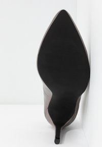 Escarpin à bout pointu, en cuir taupe lisse, avec une semelle noire élégante et un fin talon aiguille.