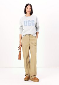 Light gray sweatshirt with blue "UGG" logo, paired with beige wide-leg trousers. Brown handbag and tan platform shoes complete the outfit.