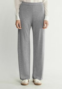 Ljusgrå vida byxor i ett mjukt, texturerat material med en platt midja. Matchas med vita sneakers med beige detaljer.