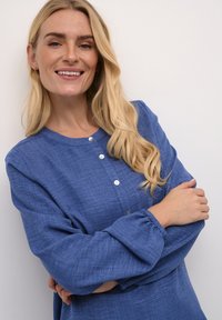 Blauwe, knoopsluiting jurk met een ronde halslijn en lange mouwen met elastische manchetten. Gemaakt van textuurstof, met een relaxte pasvorm.