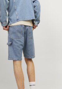 Shorts in denim blu chiaro con taglio dritto, cuciture visibili, due tasche posteriori e un anello laterale per utility. Decorati con etichetta del logo.