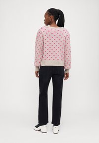 Lys pink sweater med pink polka dots, strikket tekstur og ribbede manchetter, parret med sorte bukser og hvide platform-sko.