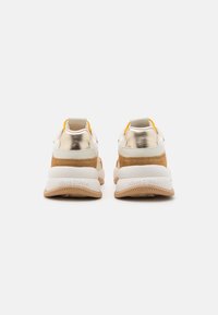 Zadní pohled na béžové a bílé tenisky se zlatými akcenty a silnými tanovými podrážkami na bílé pozadí.