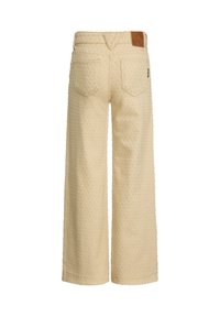 Jeans beige a gamba larga con superficie texturizzata, dotati di un design per la tasca posteriore e di un'etichetta in pelle marrone sulla vita.