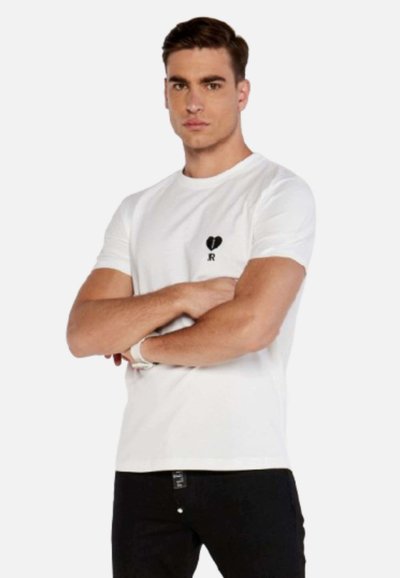 T-shirt bianca in cotone con scollatura rotonda, maniche corte, caratterizzata da un cuore nero e dal logo 'R' sul lato sinistro del petto. Indossata con jeans neri.