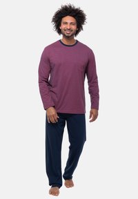 Camicia a maniche lunghe color bordeaux a righe con colletto blu, abbinata a pantaloni blu, realizzata in tessuto morbido, indossata a piedi nudi.