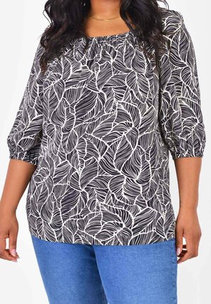 Vrouw draagt een zwart-witte blouse met bladerenpatroon, driekwart mouwen en een blauwe spijkerbroek.