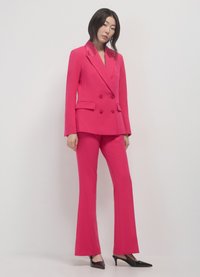 Fuchsia double-breasted blazer with glossy lapels, paired with matching flared trousers and pointed black heels. Smooth fabric, tailored fit.