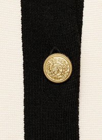 Mustavalkoinen teksturoitu kangas, jossa on näyttävä kultakoristeinen nappi, jossa on monimutkainen kuvio ja kohokuviointi.