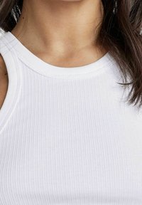 Top in cotone bianco a coste con scollo rotondo e spalline larghe, realizzato in un tessuto elasticizzato che si adatta al corpo.