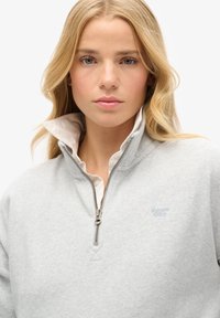Lichtgrijze zip-up sweatshirt met een hoge kraag, voorzien van een witte binnenkraag en een klein blauw logo op de borst. Zacht, textuurstof.