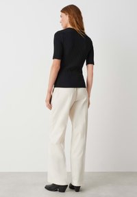 Top corto a righe nere con maniche corte abbinato a pantaloni palazzo crema e scarpe con tacco nere, visto da dietro su uno sfondo neutro.