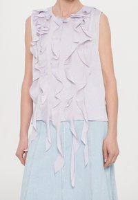 Ärmlös lila topp med lager på lager av fallande volanger, tillsammans med en ljusblå denimkjol, visad från axlarna till höfterna.