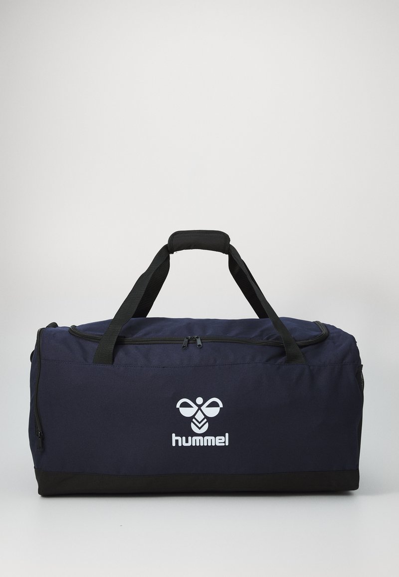 Tumed sinine spordikott mustade aksessuaaridega, valmistatud vastupidavast kangast, varustatud lukuga pealmise osaga, kahe käepideme ja silmapaistva suure valge logoga.