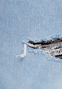 Ljust blå denimtyg med en horisontell reva som avslöjar vita och svarta randiga trådar under samt fransade kanter.